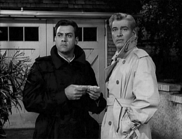 Perry and Paul in raincoats, outside a garage at night